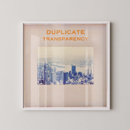 The image is a framed photograph of a cityscape, with the text "DUPLICATE TRANSPARENCY" written above it.