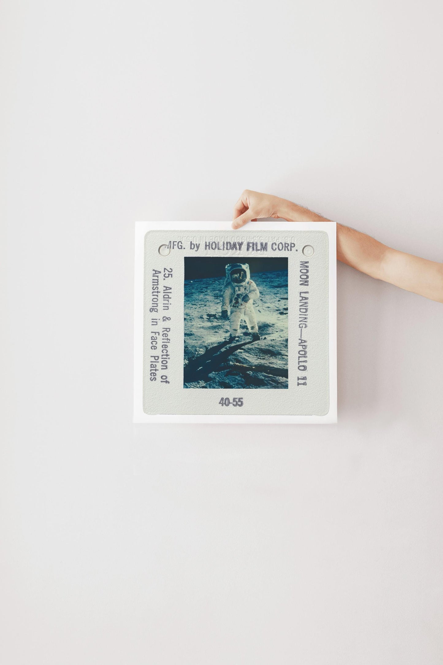 A person's hand is holding a framed photograph of an astronaut on the moon, with the text "F.C. by HOLIDAY FILM CORP. Moon Landing Apollo 11" visible.