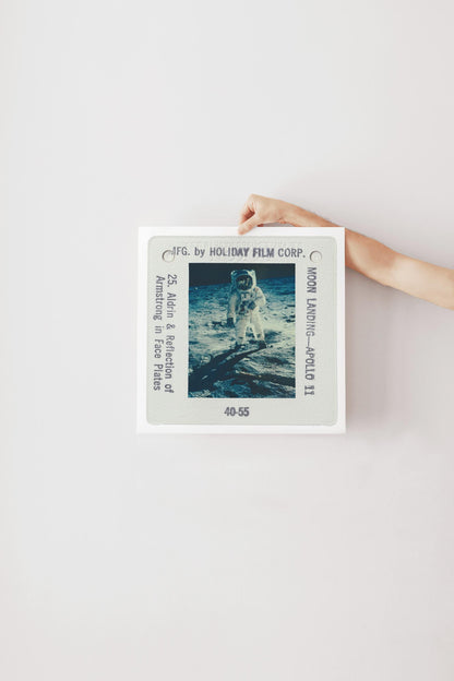 A person's hand is holding a framed photograph of an astronaut on the moon, with the text "F.C. by HOLIDAY FILM CORP. Moon Landing Apollo 11" visible.
