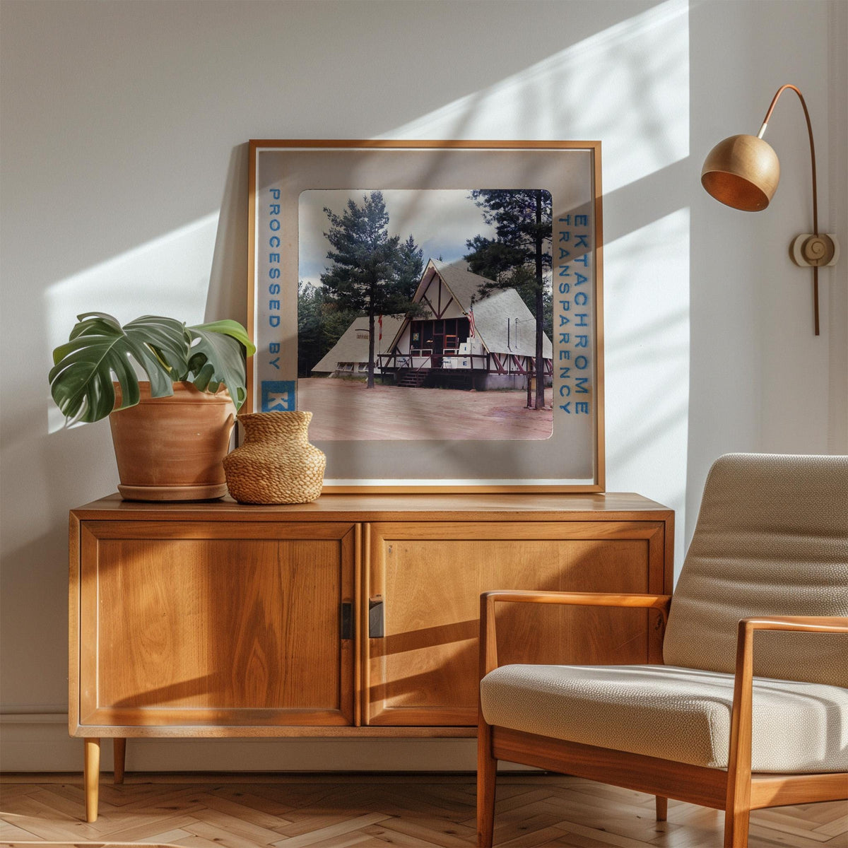 a wooden cabinet with a framed photograph of a building, a potted plant, and a woven basket on top. The photograph is framed in a wooden frame and hangs on a white wall.