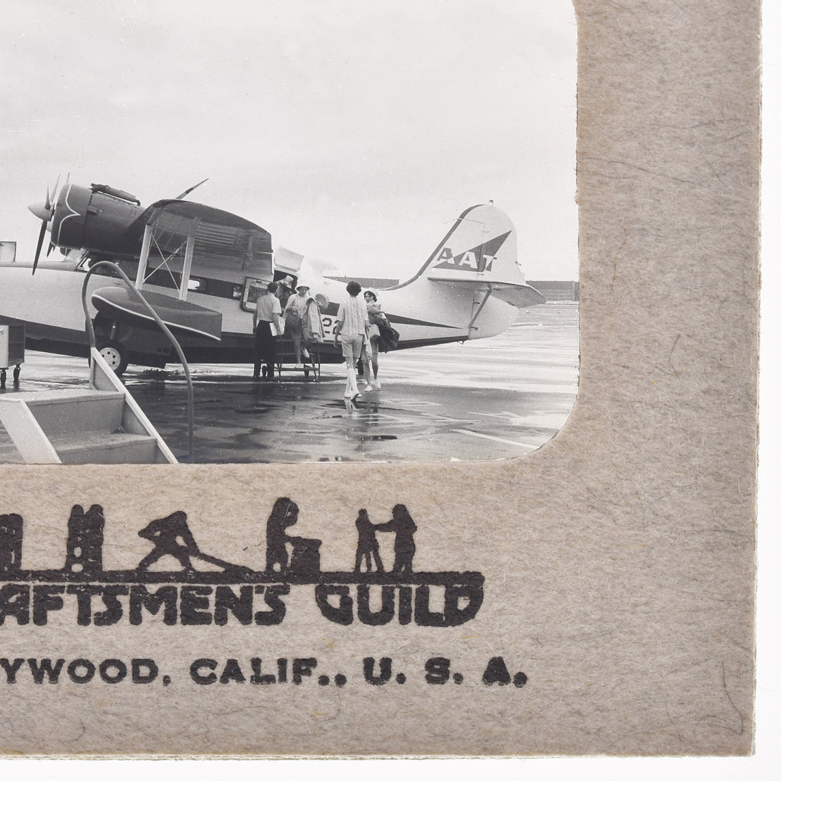 a group of people boarding a small airplane on a wet tarmac, with the text "Craftsmen's Guild" and "YWOOD, CALIF. U.S.A." printed on the side of the photo.