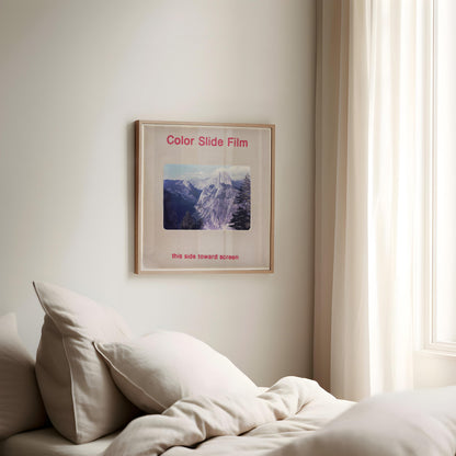a bedroom with a bed, a framed poster of a mountain landscape, and a window with curtains.