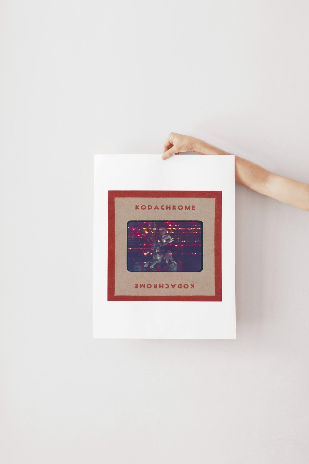 A person's hand is holding a framed poster with the text "KODACHrome" on it.
