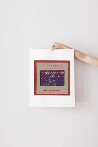 A person's hand is holding a framed poster with the text "KODACHrome" on it.