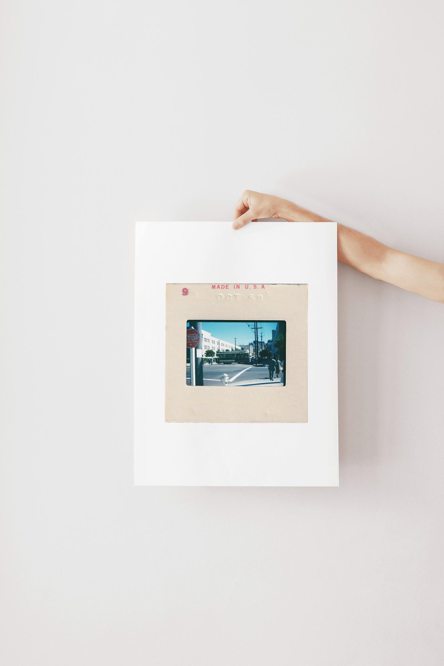 Vintage 1958 Kodachrome slide photograph of a San Francisco cable car passing through a sunny city intersection, with pedestrians in period dress, a red stop sign, utility poles, and a bright blue autumn sky. Printed as a giclée fine art print on archival matte paper.