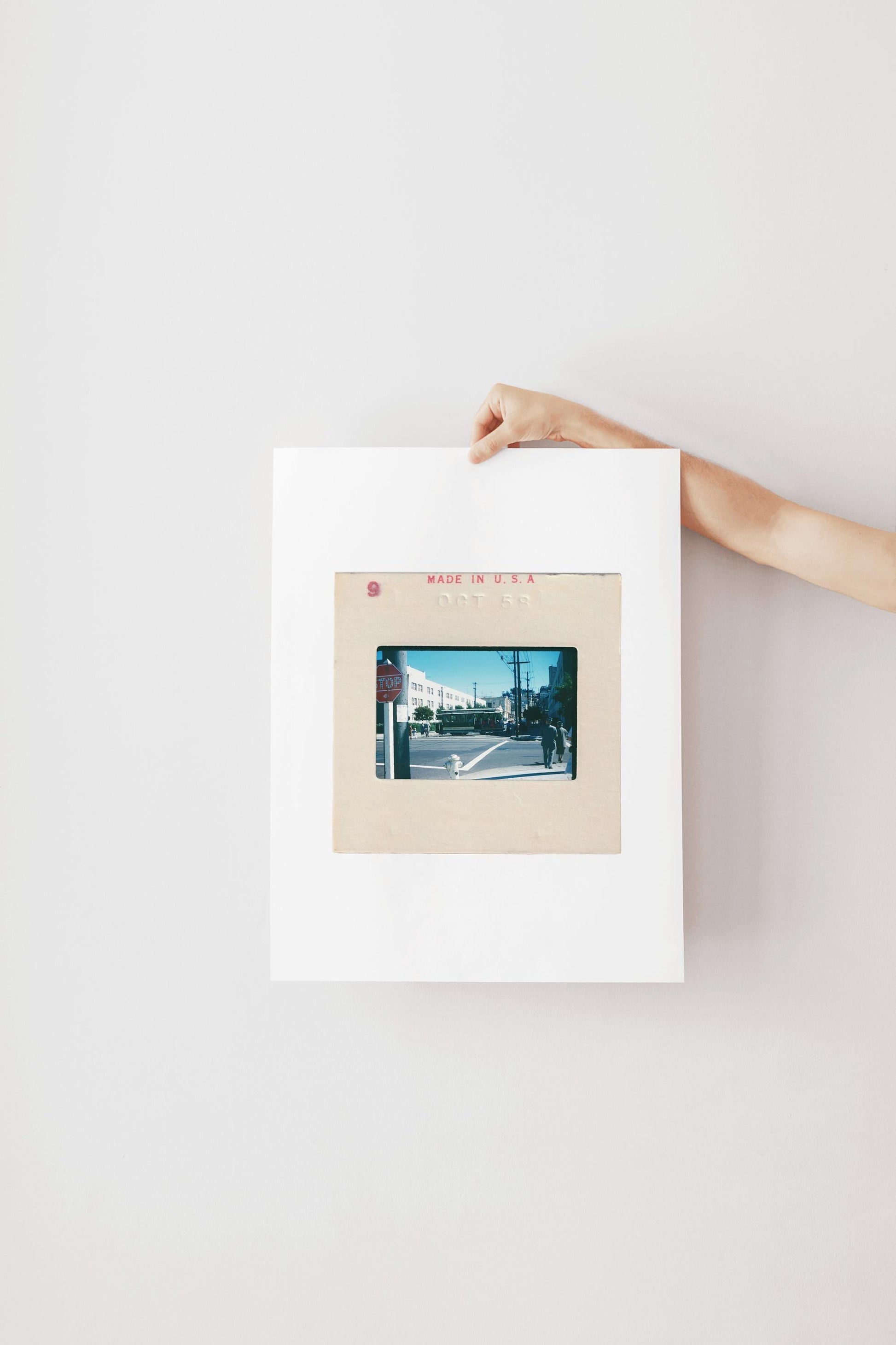 Vintage 1958 Kodachrome slide photograph of a San Francisco cable car passing through a sunny city intersection, with pedestrians in period dress, a red stop sign, utility poles, and a bright blue autumn sky. Printed as a giclée fine art print on archival matte paper.