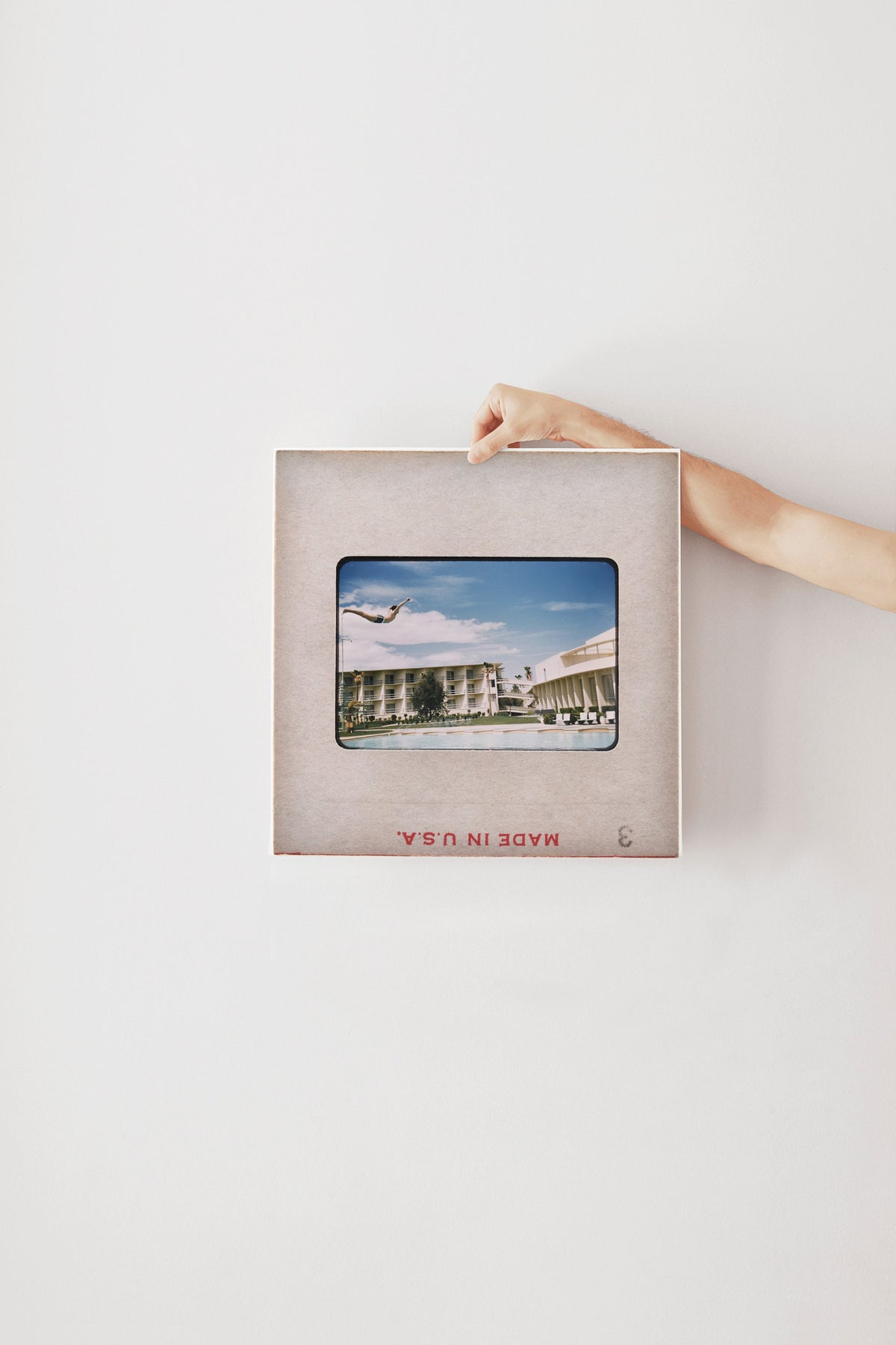A hand is holding a framed photograph of a building with a plane flying overhead.