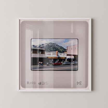 The image is a framed photograph of a city street scene with buildings, cars, and people.