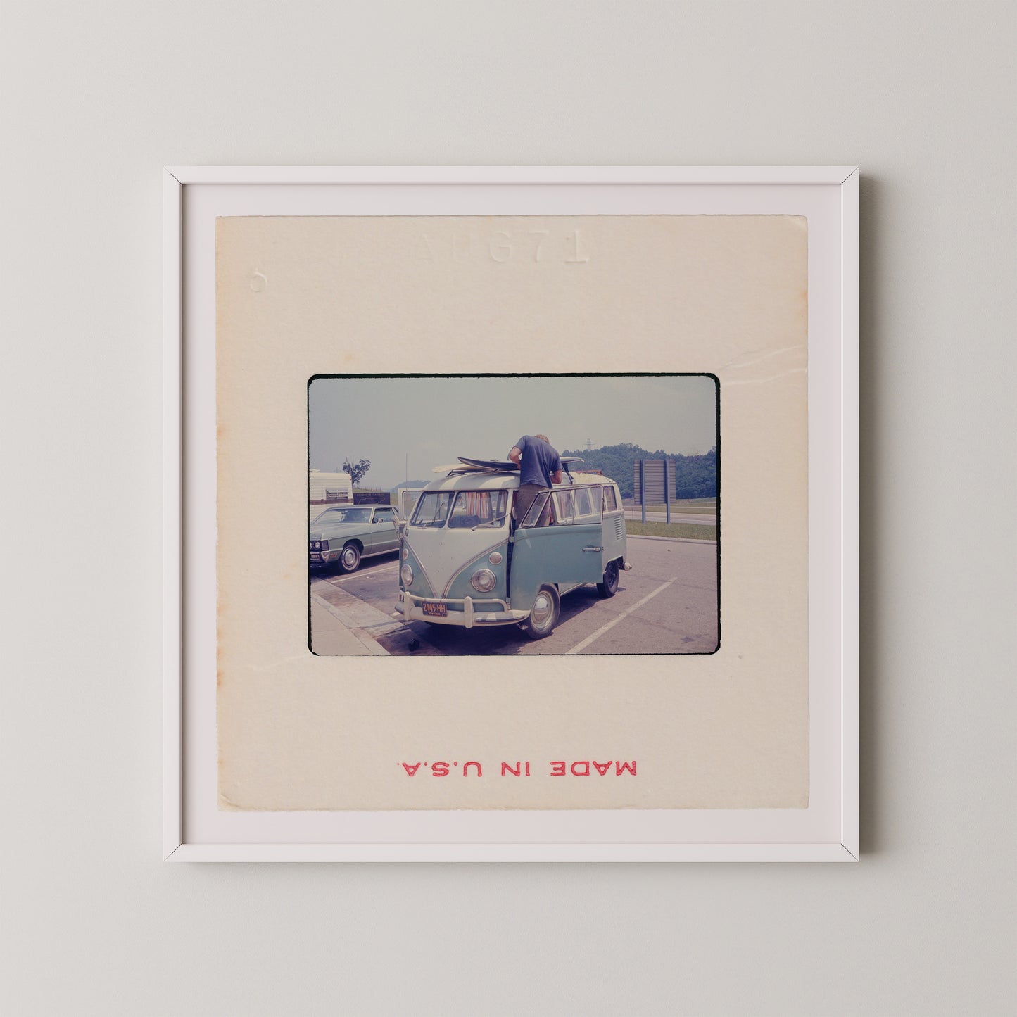 A vintage photograph of a blue Volkswagen van parked in a parking lot, with a person standing on the van's hood.
