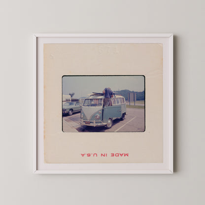 A vintage photograph of a blue Volkswagen van parked in a parking lot, with a person standing on the van's hood.