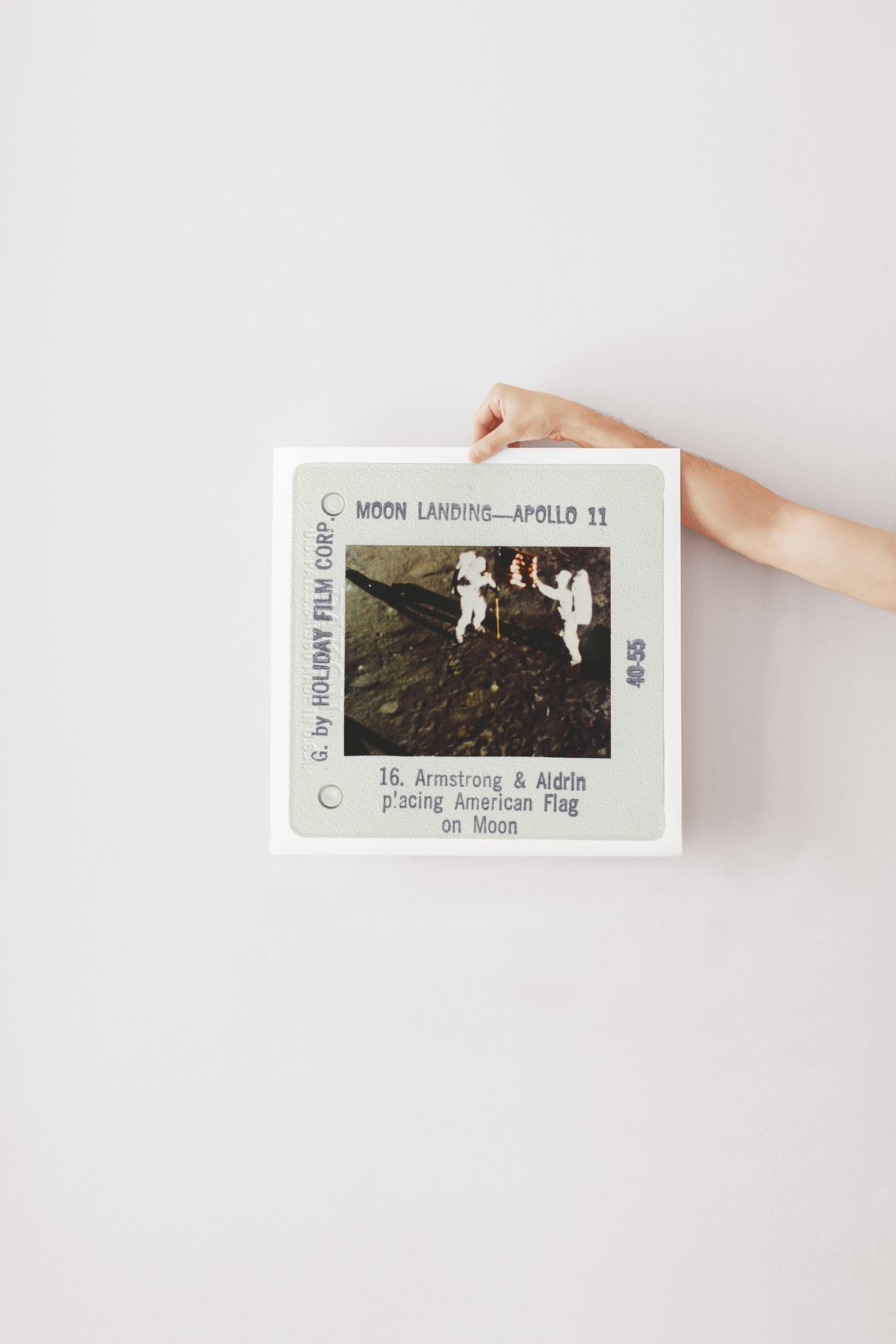 A person's hand is holding a framed photograph of the Apollo 11 moon landing, with the text "Moon Landing - Apollo 11" visible.