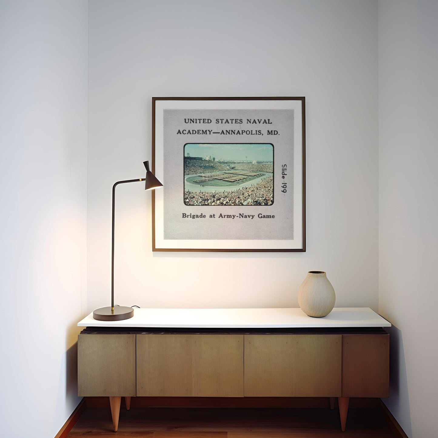 a framed vintage photograph of a baseball stadium, with a lamp and a vase on a wooden cabinet below it.