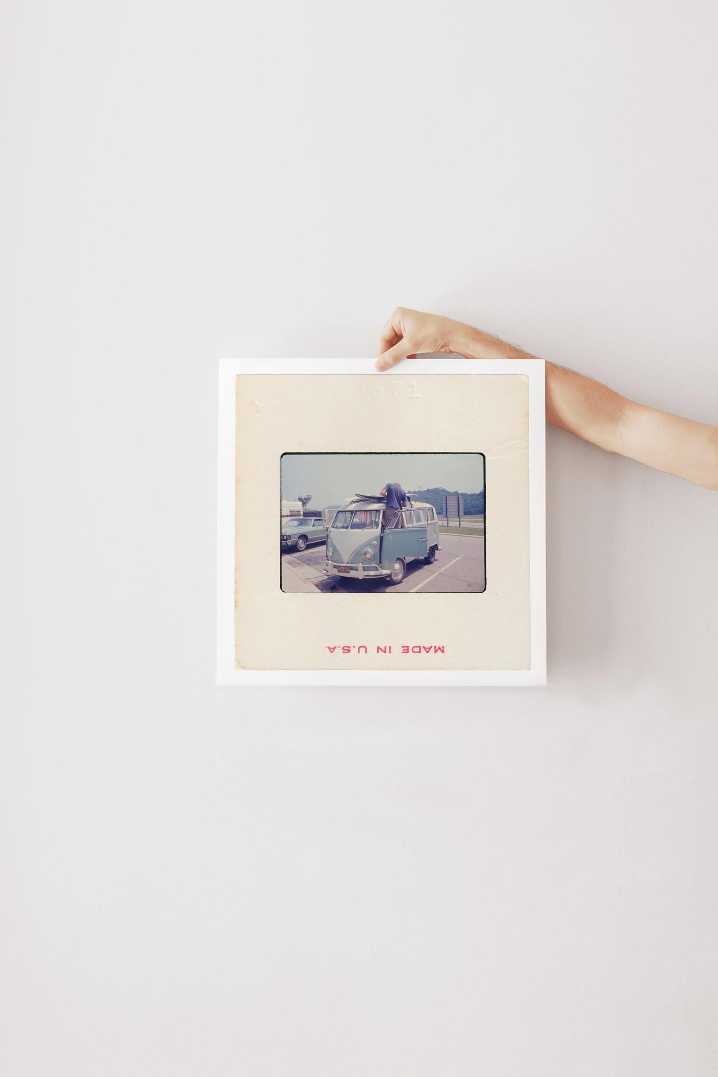 Vintage 1971 35mm slide photograph of a man loading two surfboards onto the roof rack of a pale blue Volkswagen Bus in a parking lot, with a "Welcome to Tennessee" highway sign and a vintage sedan visible in the background. Printed as a giclée fine art print on archival matte paper.