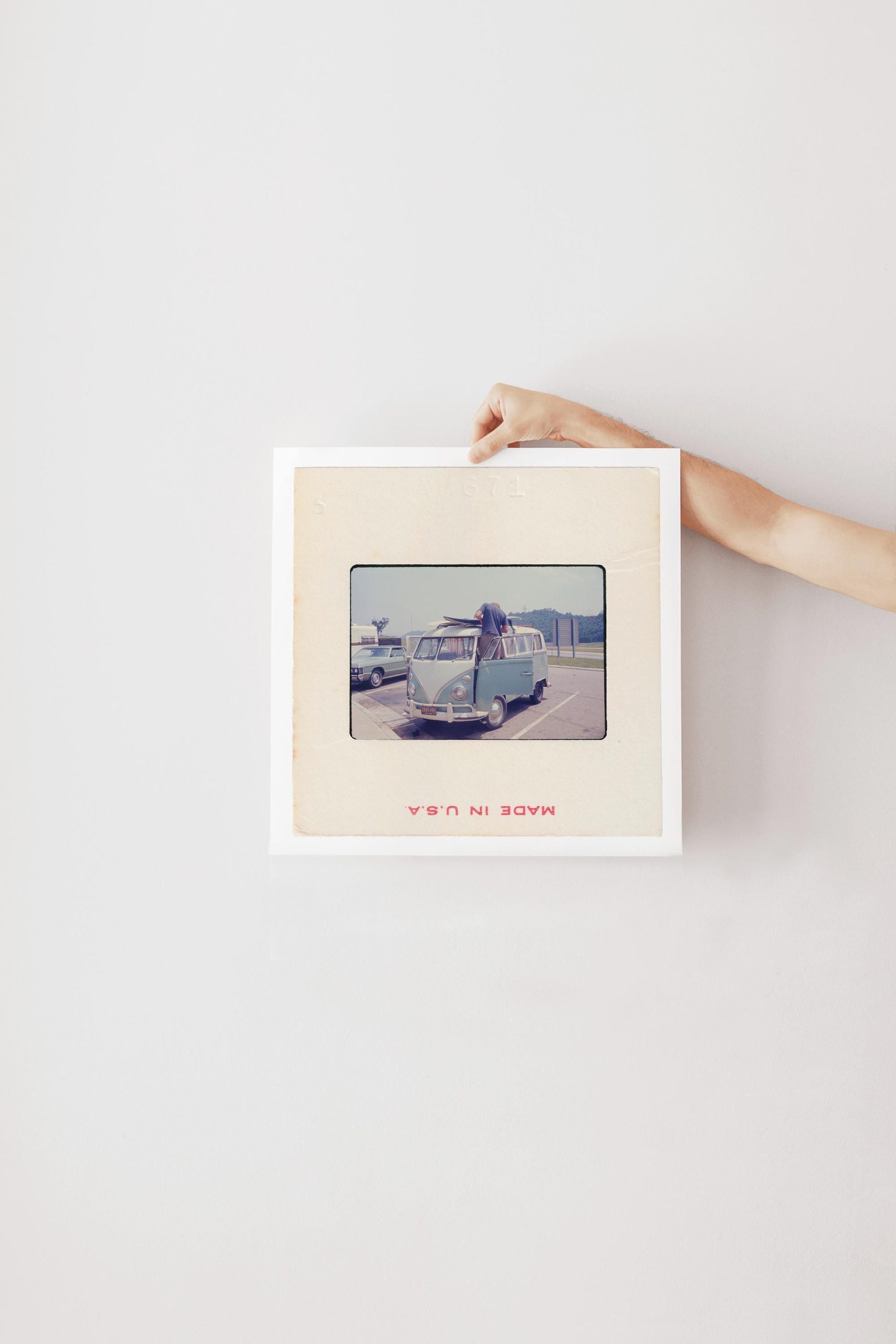 Vintage 1971 35mm slide photograph of a man loading two surfboards onto the roof rack of a pale blue Volkswagen Bus in a parking lot, with a "Welcome to Tennessee" highway sign and a vintage sedan visible in the background. Printed as a giclée fine art print on archival matte paper.