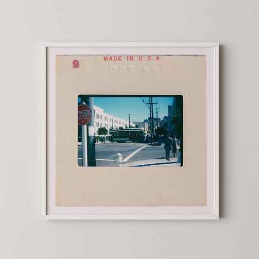 The image is a framed photograph of a street scene with a stop sign, a fire hydrant, and people walking on the sidewalk.