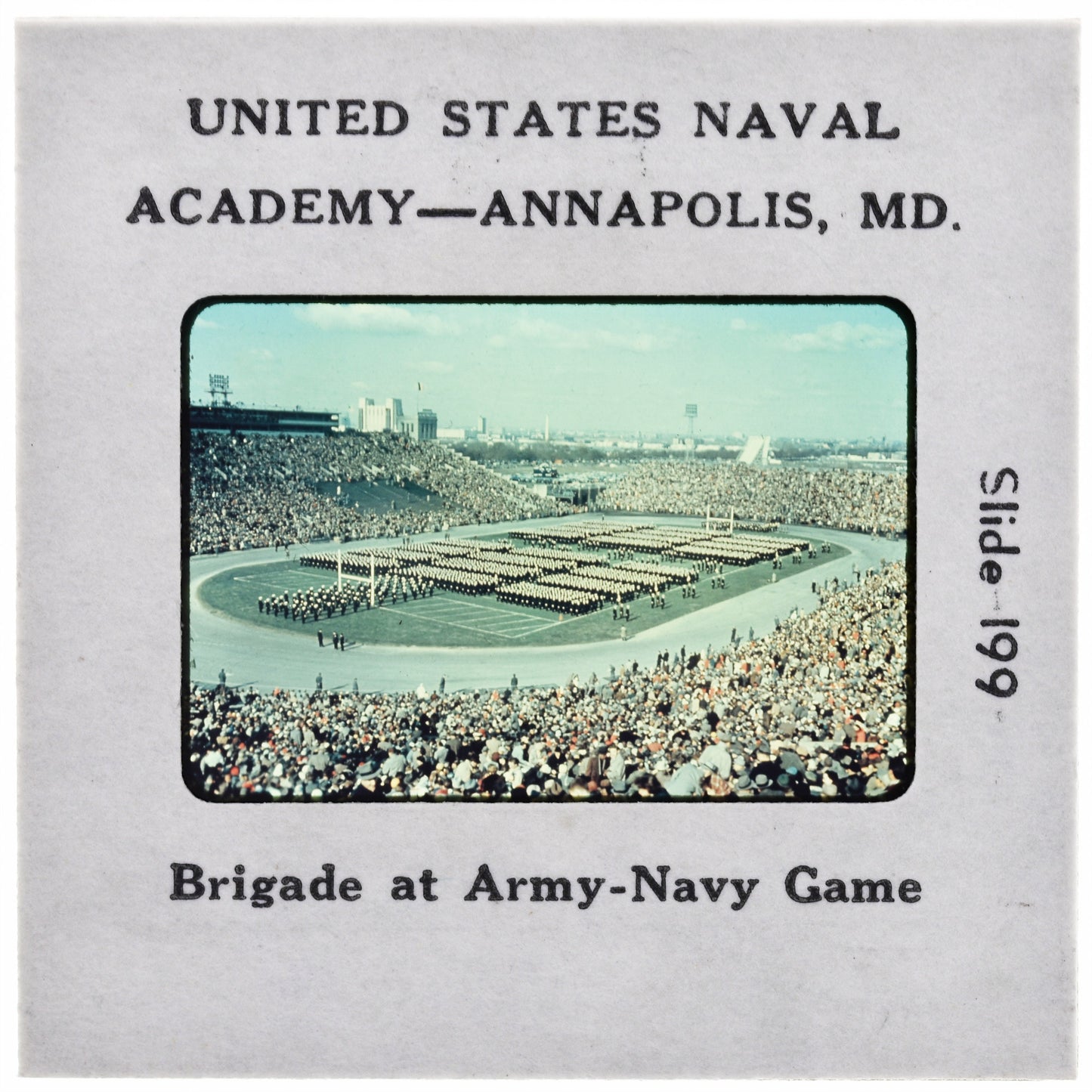 A large crowd of people gathered in a stadium, with military personnel standing in formation in the foreground.