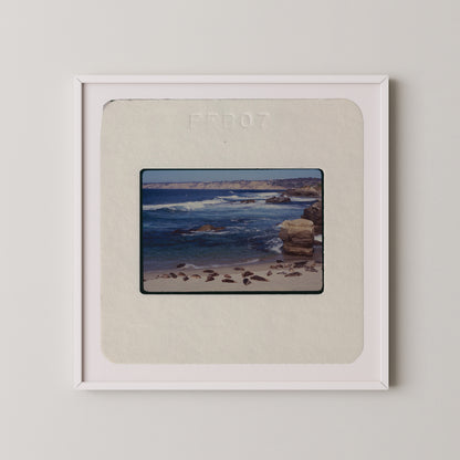 The image is a framed photograph of a beach scene with rocks and water.