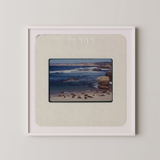 The image is a framed photograph of a beach scene with rocks and water.