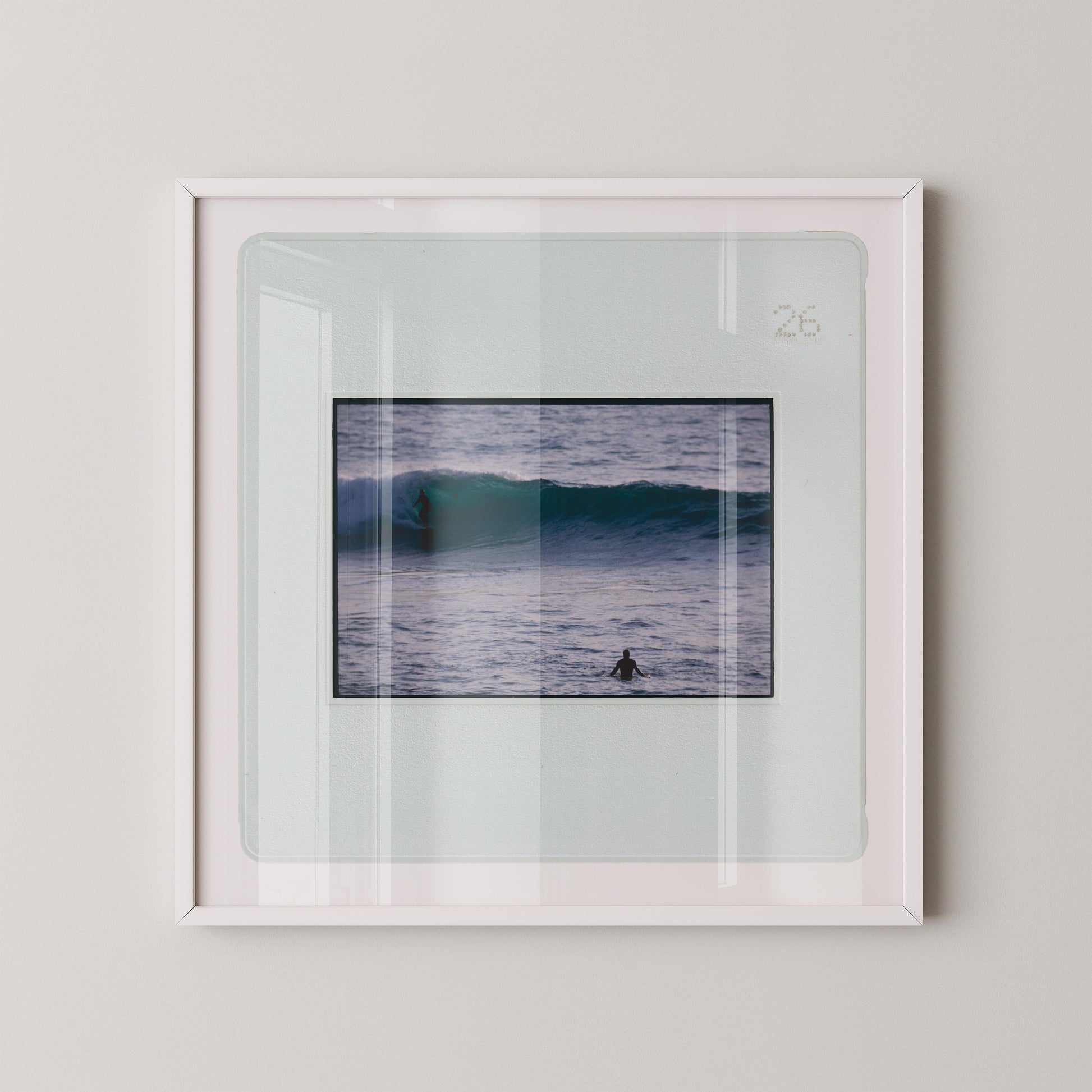 Vintage slide photograph of two surfers in the ocean — one riding a glassy teal-green wave in the background and one waiting chest-deep in silver-grey water in the foreground, shot with a telephoto lens from shore. Printed as a giclée fine art print on archival matte paper.