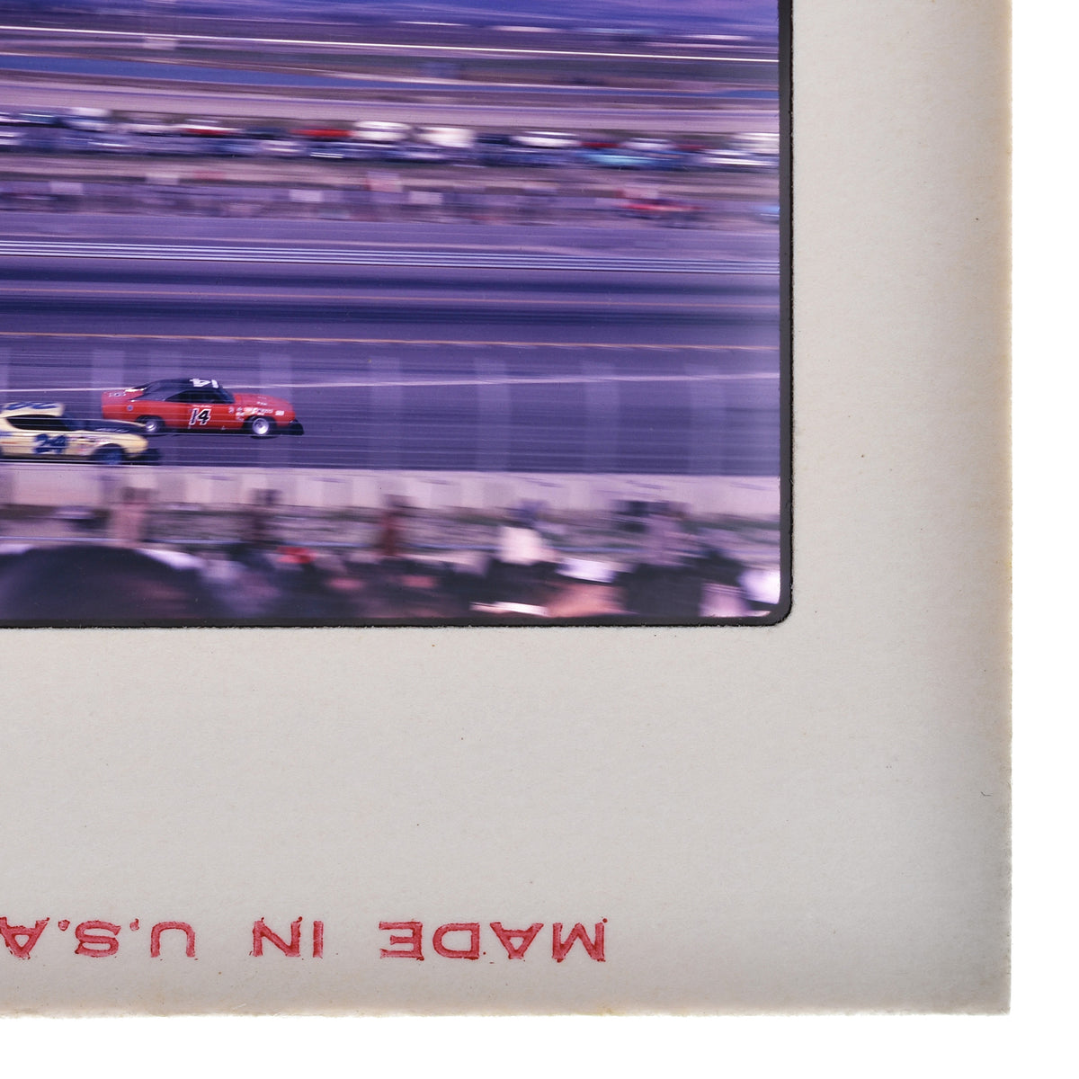 The image is a blurry photograph of a race track with multiple cars racing, and there is a red and white sign with the text "Made in Usa" visible in the frame.