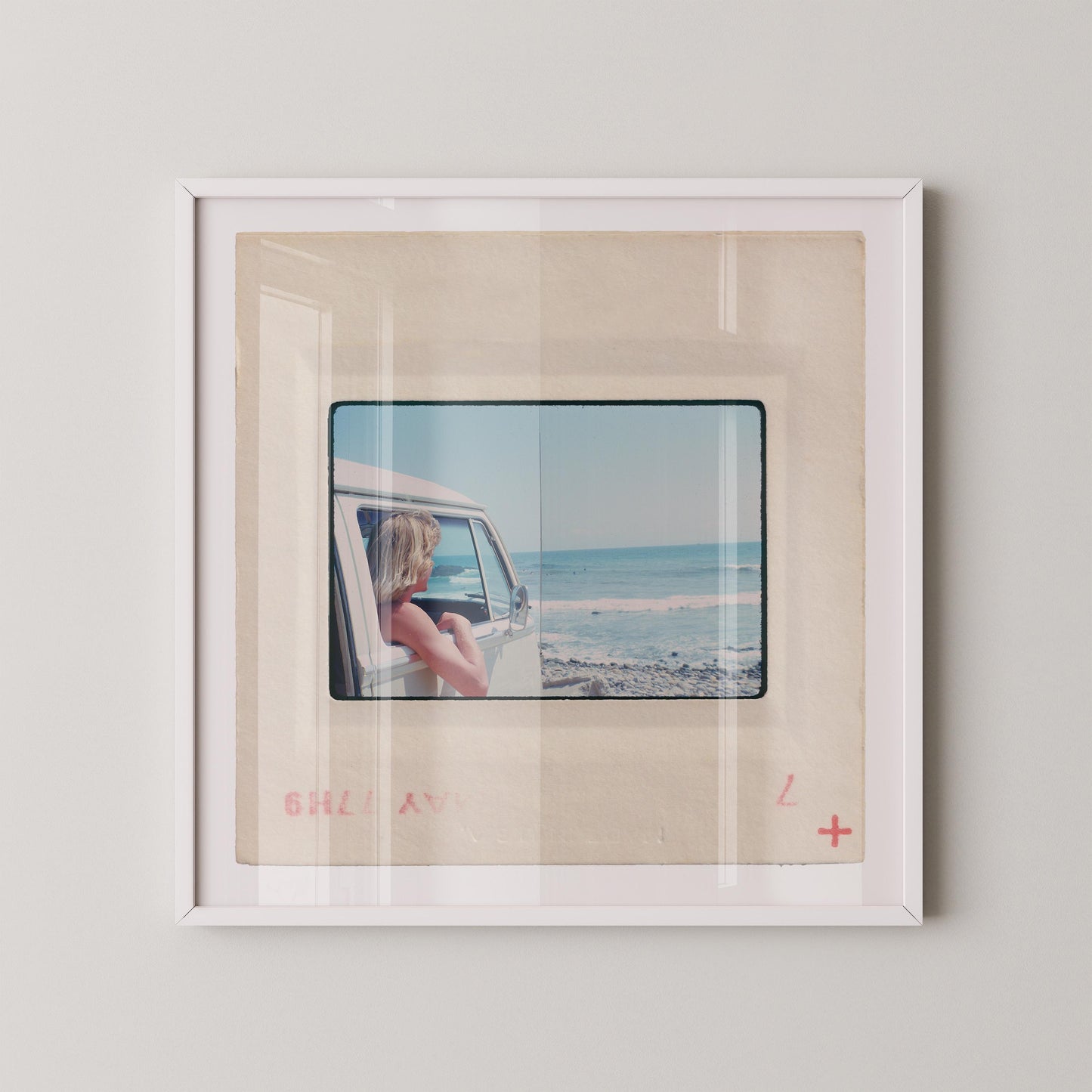 Vintage 1977 Kodachrome slide photograph of a blonde child leaning out the window of a white Volkswagen Microbus, looking toward the ocean along the California coast. Rocky shoreline and gentle surf visible in the background. Printed as a giclée fine art print on archival matte paper.