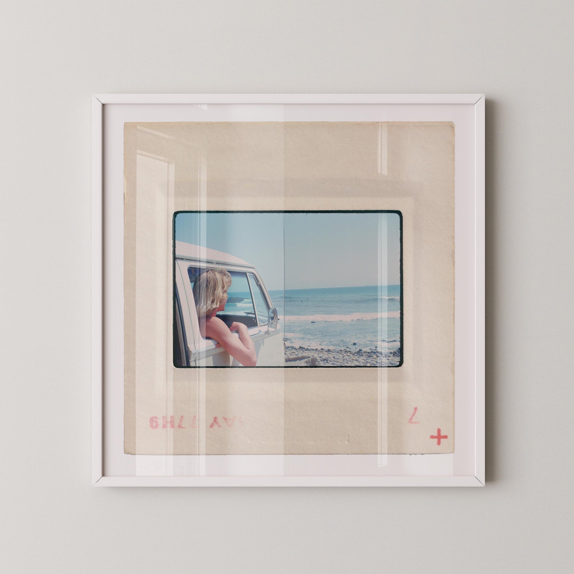 Vintage 1977 Kodachrome slide photograph of a blonde child leaning out the window of a white Volkswagen Microbus, looking toward the ocean along the California coast. Rocky shoreline and gentle surf visible in the background. Printed as a giclée fine art print on archival matte paper.