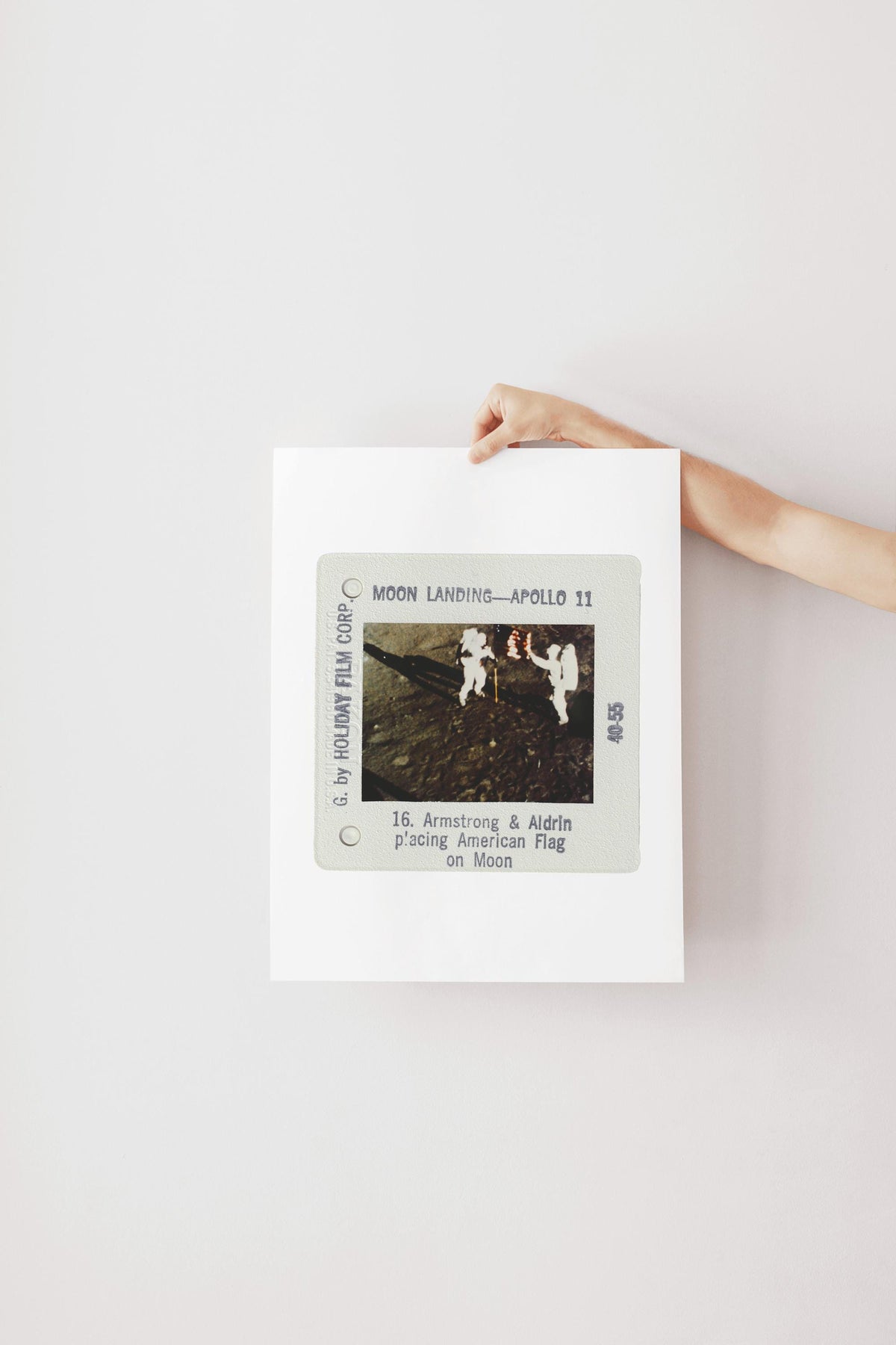 A person is holding a framed photograph of the Apollo 11 moon landing, featuring the silhouettes of the three astronauts on the lunar surface.