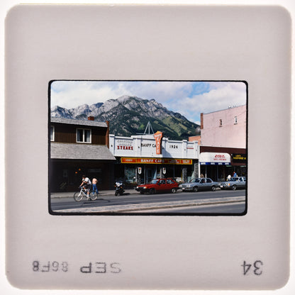 A small town street with a movie theater, a red car, and a mountain in the background.