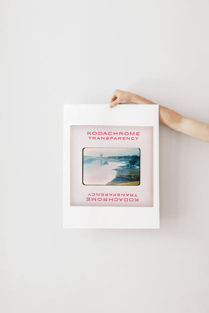 A person's hand is holding a framed photograph of a scenic landscape, with the text "Kodachrome transparency" visible on the frame.