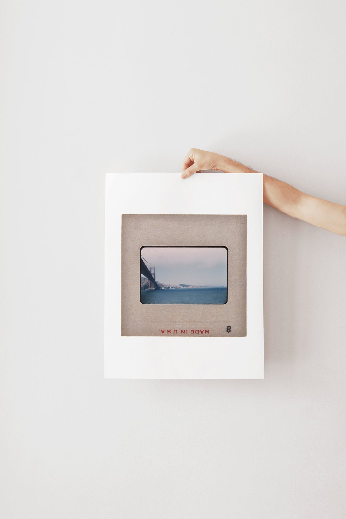 A person's hand is holding a white frame with a framed photograph of a bridge in the background.