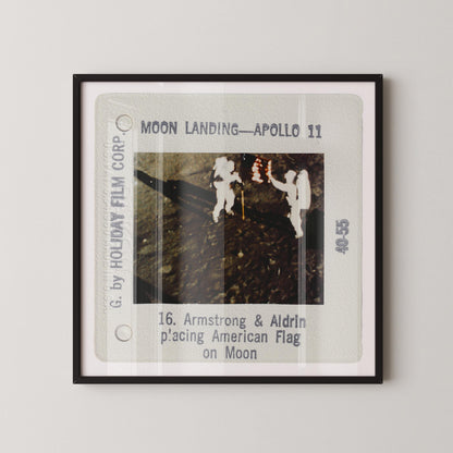 The image is a framed photograph of two people in white suits standing on the moon's surface, with the text "Moon Landing - Apollo 11" and "16. Armstrong & Aldrin p'acting American Flag on Moon" visible.