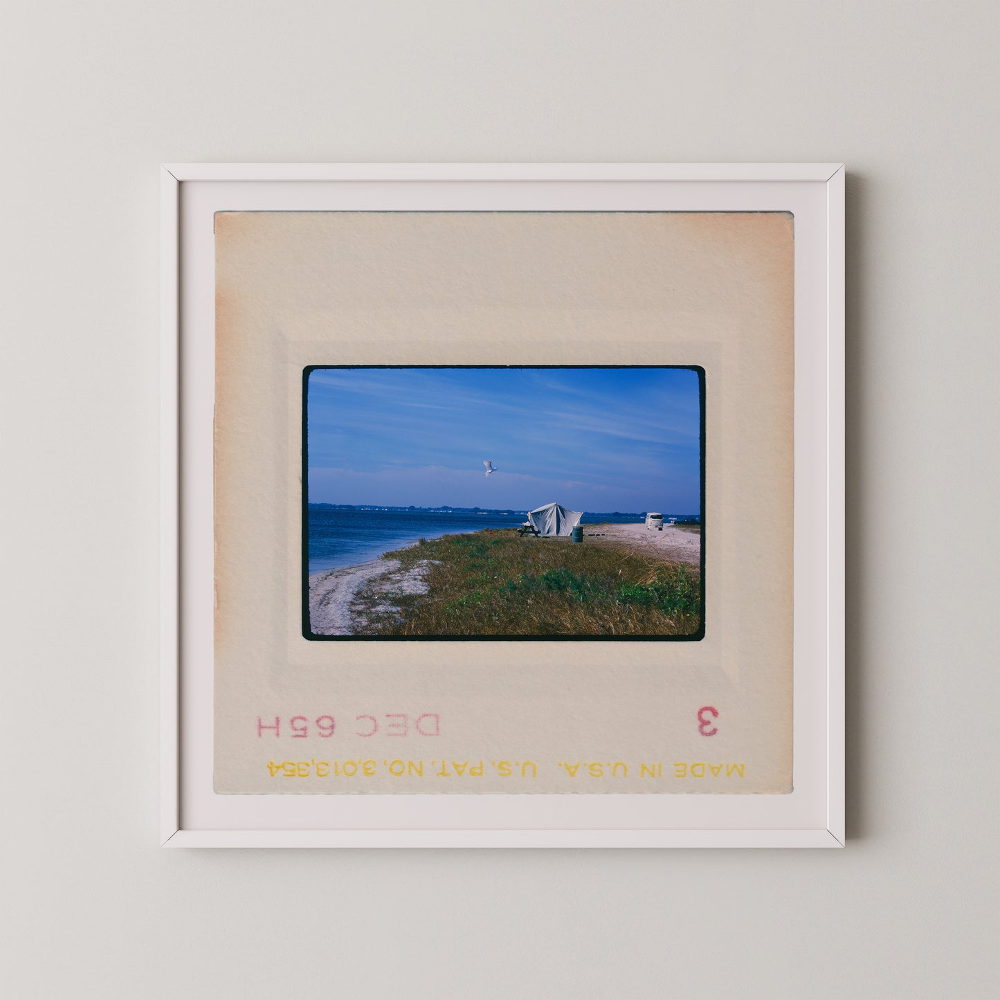 A framed photograph of a beach scene with a small building and a kite in the sky.