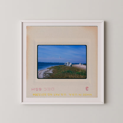 A framed photograph of a beach scene with a small building and a kite in the sky.