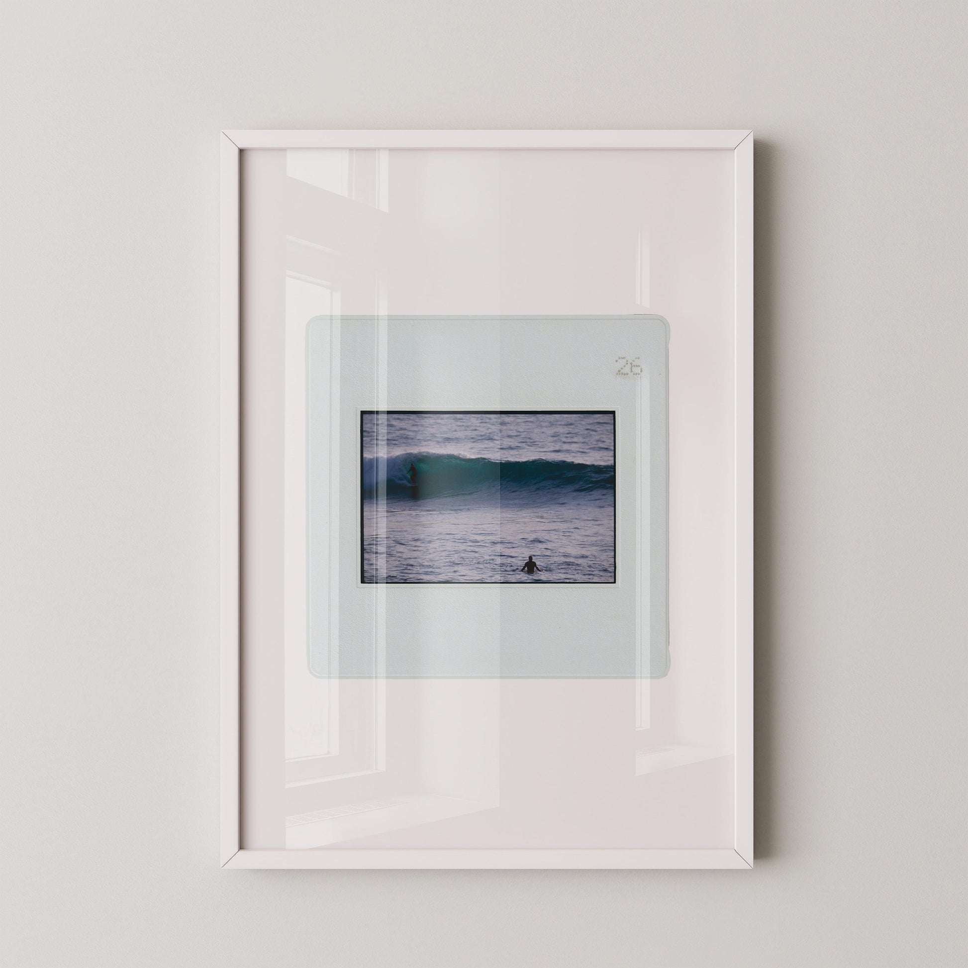 Vintage slide photograph of two surfers in the ocean — one riding a glassy teal-green wave in the background and one waiting chest-deep in silver-grey water in the foreground, shot with a telephoto lens from shore. Printed as a giclée fine art print on archival matte paper.