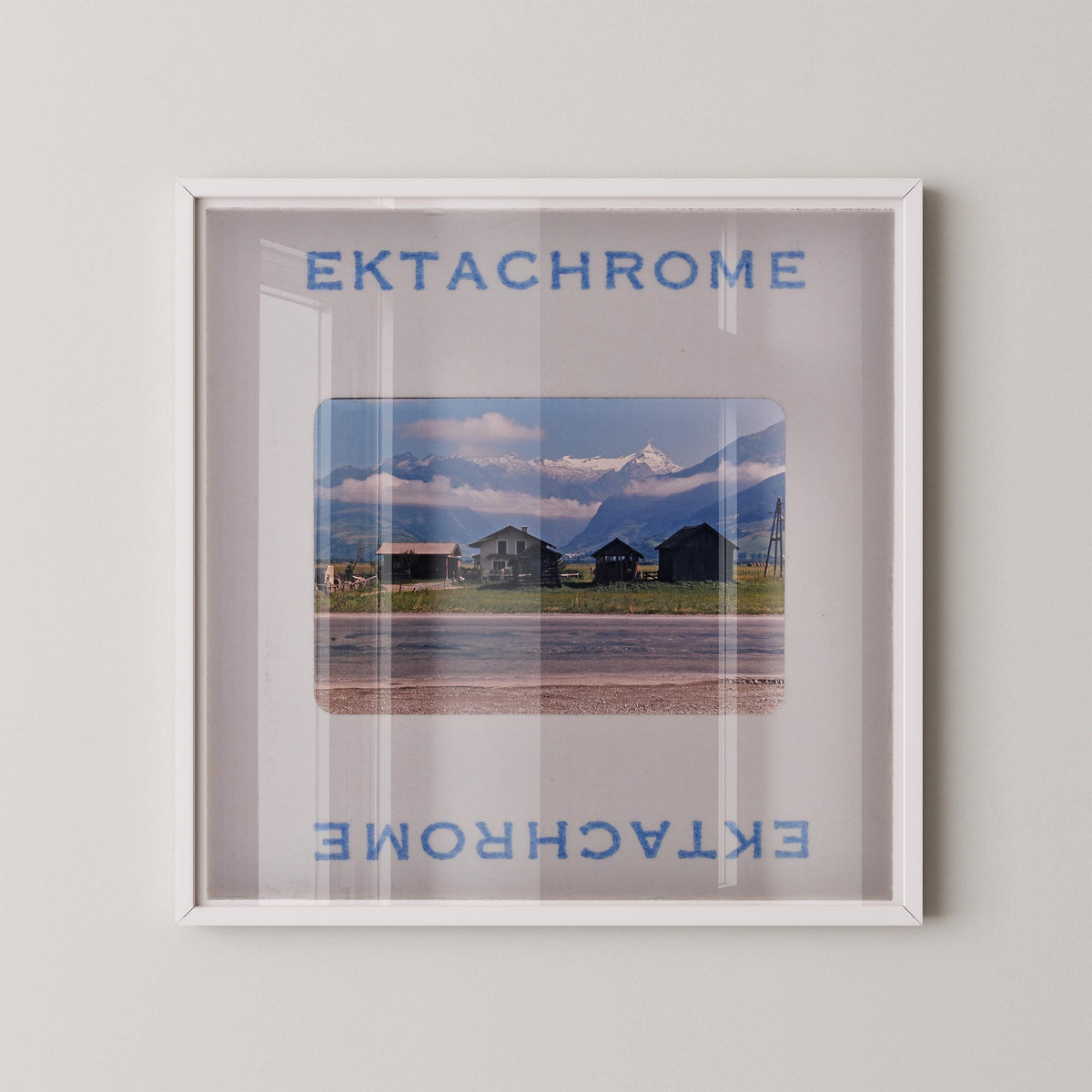 The image is a framed photograph of a scenic mountain landscape, with a clear glass frame that allows the viewer to see the mountain and the surrounding area.
