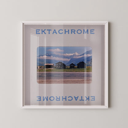 The image is a framed photograph of a scenic mountain landscape, with a clear glass frame that allows the viewer to see the mountain and the surrounding area.