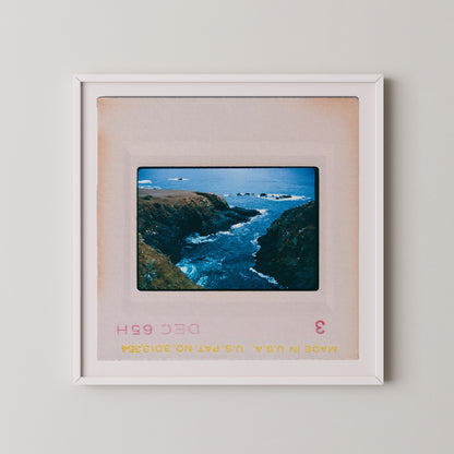 The image is a framed photograph of a scenic coastal landscape with rocky cliffs, crashing waves, and a vast expanse of blue ocean.