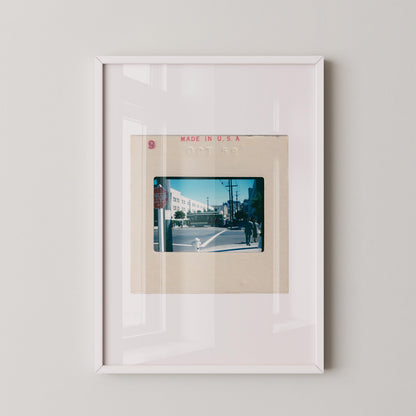 Vintage 1958 Kodachrome slide photograph of a San Francisco cable car passing through a sunny city intersection, with pedestrians in period dress, a red stop sign, utility poles, and a bright blue autumn sky. Printed as a giclée fine art print on archival matte paper.