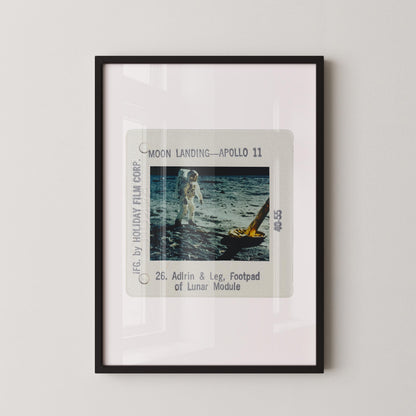 The image is a framed photograph of an astronaut walking on the surface of the moon, with a yellow spacecraft visible in the background.