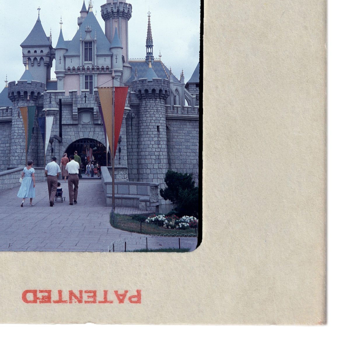 A group of people walking in front of a castle-like structure, with flags and flowers visible in the foreground.