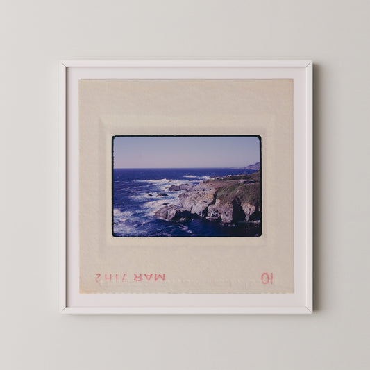 The image is a framed photograph of a rocky coastline with crashing waves, depicting a scenic coastal landscape.