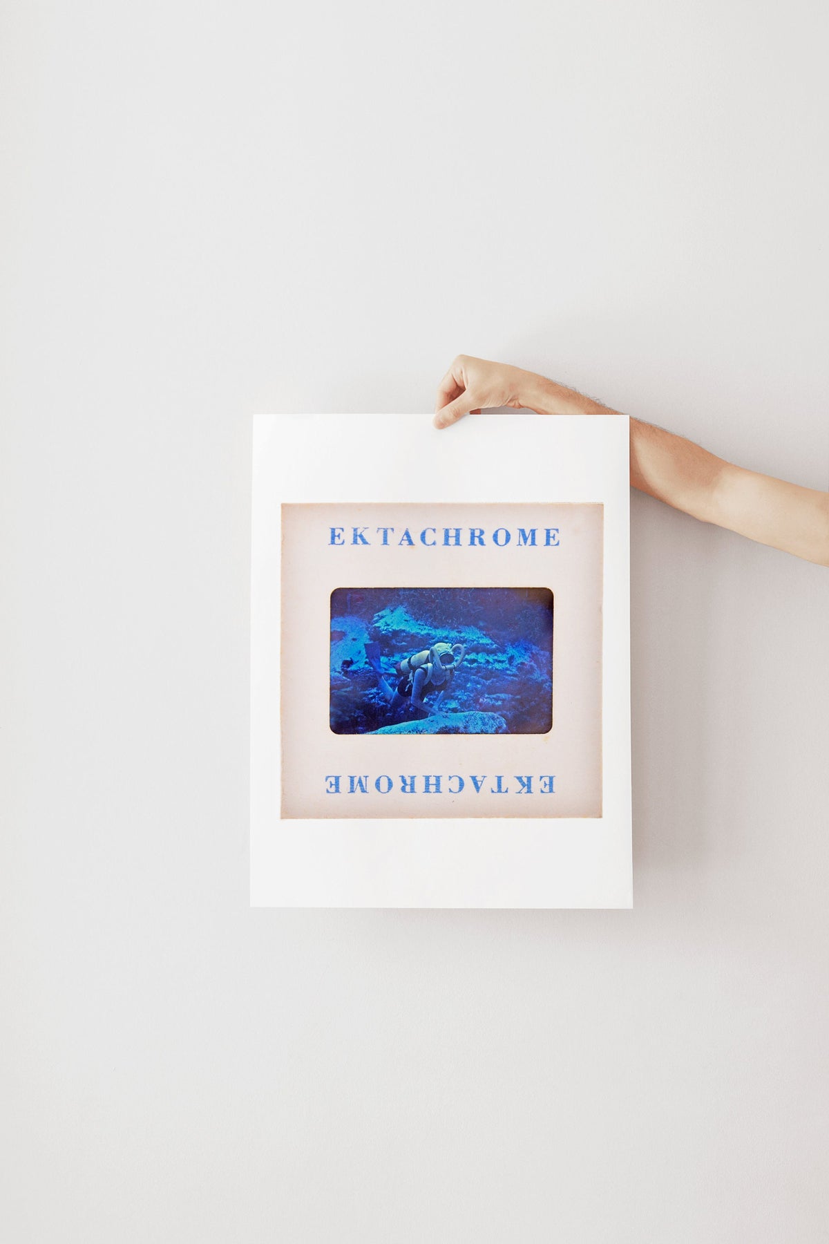A person's hand is holding a framed image with the text "Ek Tachrome" on it.