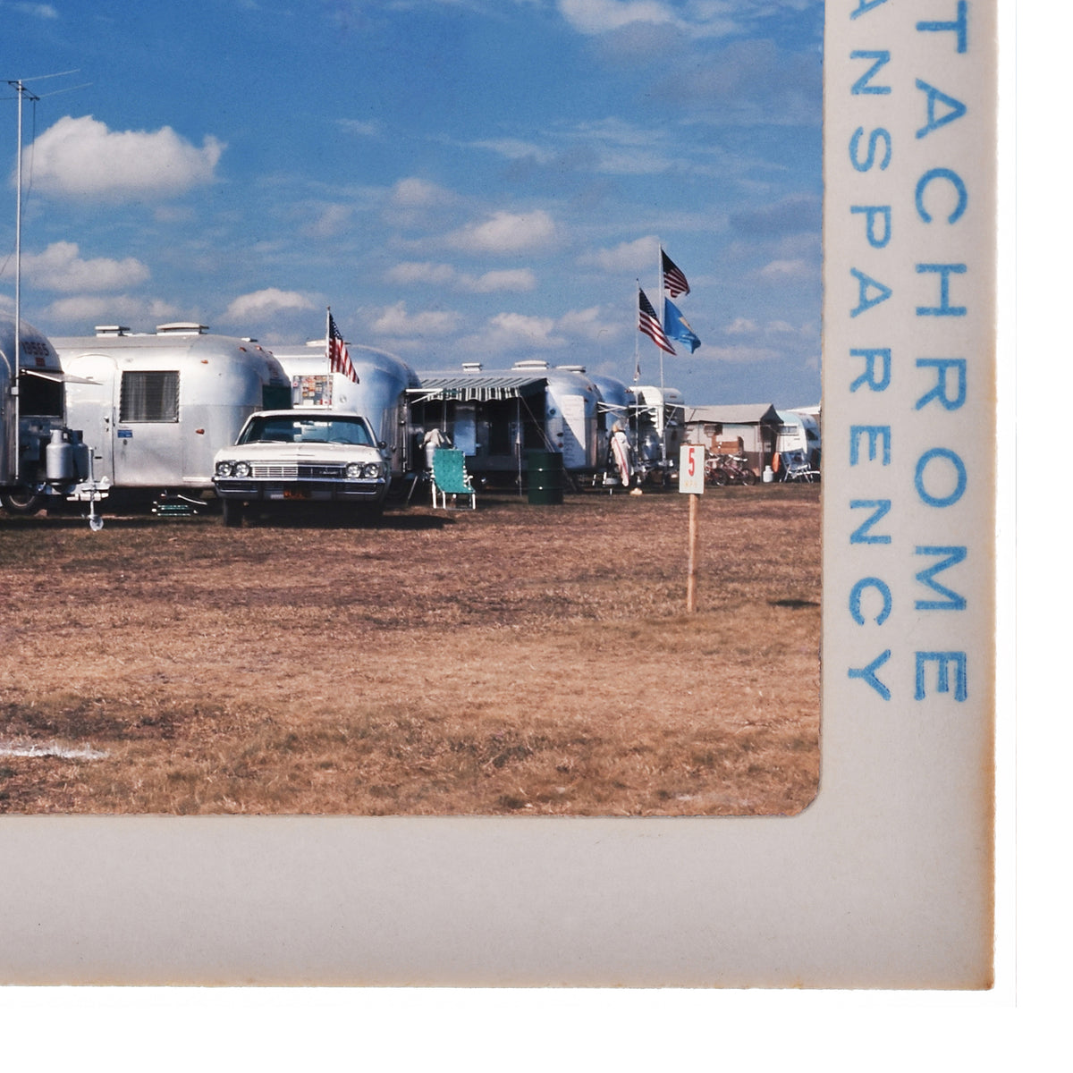 A collection of trailers and vehicles parked in a field, with American flags flying in the background.