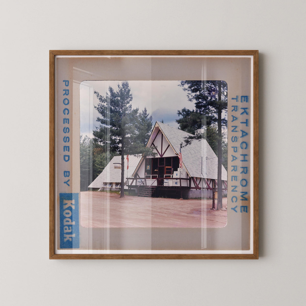 A framed photograph of a white building with a triangular roof, surrounded by trees, with the text "Kodak" visible on the frame.
