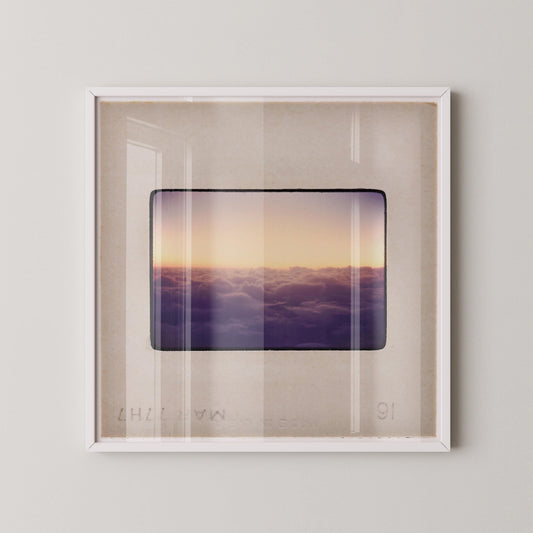 The image is a framed photograph of a sunset over a cloudy sky, with the sun setting behind the clouds.