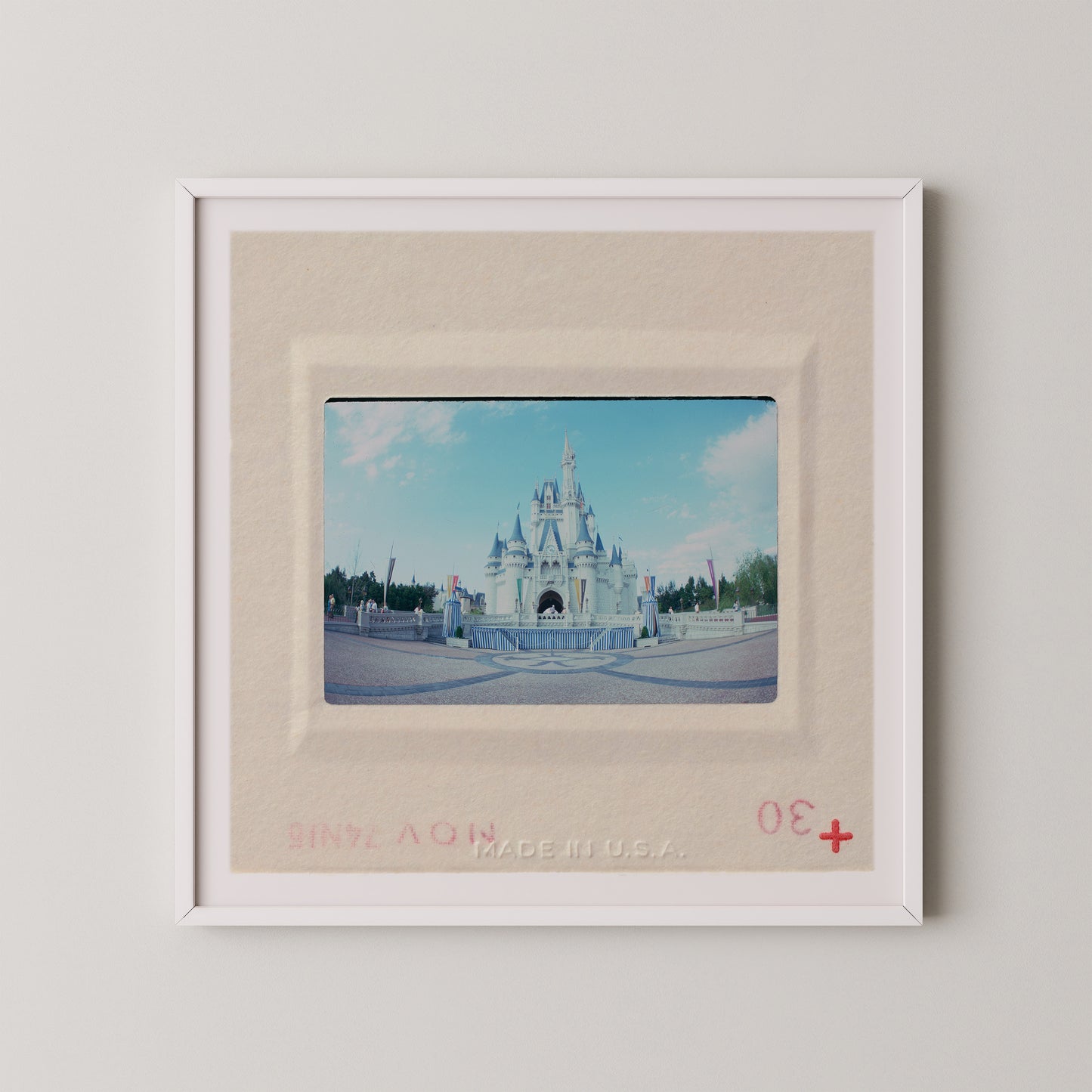 A framed photograph of a castle, likely from a theme park or tourist attraction, with a red border and a red plus sign in the bottom right corner.