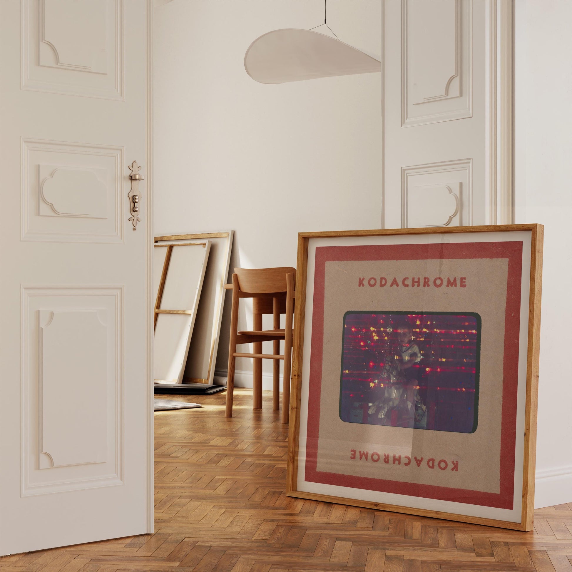 a framed artwork with a red border and the word "KODACHrome" written on it, placed on a wooden floor in a room with white walls.