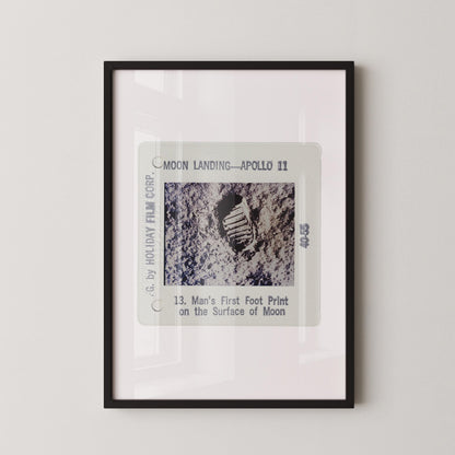 The image is a framed photograph of a man's first footprint on the surface of the moon, taken during the Apollo 11 mission.