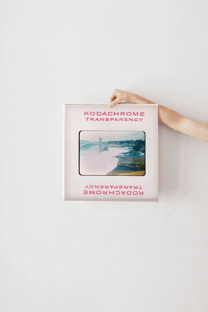 A hand is holding a framed photograph of a waterfall, with the text "KODACHrome Transparency" visible on the frame.