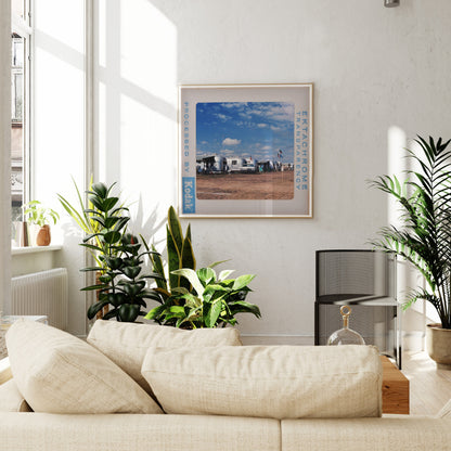 a cozy living room with a beige sofa, a framed picture of a beach scene, and several potted plants.